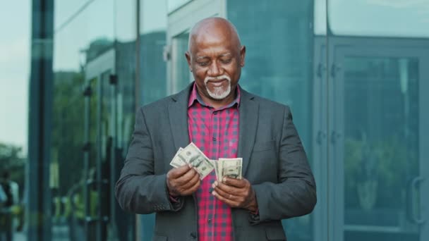 紙幣を数えるドルの山を持つ成熟した男。男性の手にドル紙幣を使用してください。成功と富のビジネスコンセプト。幸せなアフリカ系アメリカ人の高齢者が購入するお金の数を引退 — ストック動画