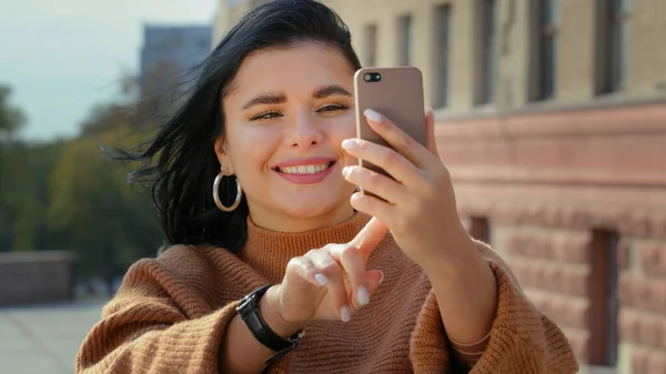 Zbliżenie szczęśliwy młoda kobieta w mieście na zewnątrz bierze selfie dotyka ekran komunikowanie przez wideo rozmowy online z telefon gadżet ładna Latynoska dziewczyna blogger rozmowy uśmiechnięta konferencja przez telefon urządzenie — Zdjęcie stockowe