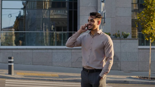 Молодий щасливий усміхнений успішний бізнесмен бородатий хлопець бос керівник стоїть в місті на вулиці розмовляючи на мобільному телефоні, відповідаючи на дзвінок віддаленої розмови переговорів за допомогою смартфона на відкритому повітрі — стокове фото