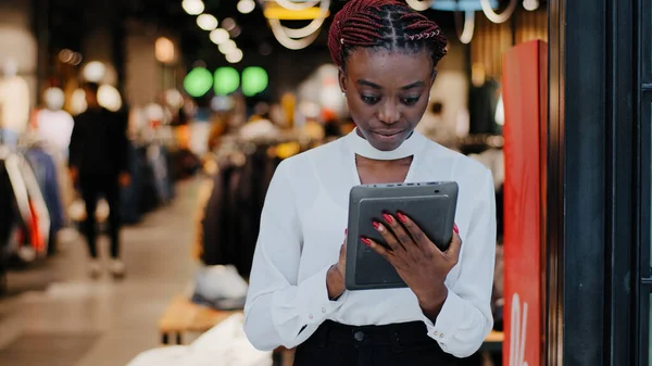 Afroamericano serio successo venditore donna consulente in negozio di abbigliamento boutique dipendente guarda tablet digitale fa inventario contabilità opere on-line legge informazioni sconto — Foto Stock