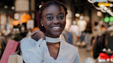 Kara Cuma konsepti. Gülümseyen, alışveriş meraklısı, mutlu, Afro-Amerikalı bir kadın, alışveriş merkezinden alışveriş poşetleri alan, mağazada duran heyecanlı bir kız. Büyük indirimlerden kıyafet alıyor, düşük fiyatlı portreler satıyor.