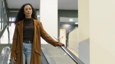 Uzun kıvırcık saçlı esmer, esmer, ciddi bir iş kadını. Müşteri müşterisi. Alışveriş merkezinin ofisindeki merdivenlerde yürüyen yürüyen merdiven.