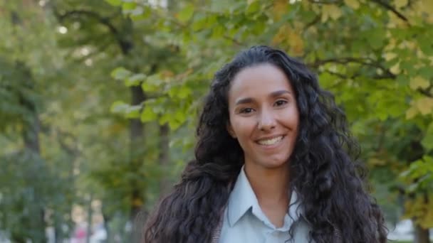 Close-up mujer hermosa satisfecha hermosa chica joven hispana dama morena con el pelo rizado largo con maquillaje natural de pie posando en el parque al aire libre sonrisa sonriente mirando a la cámara — Vídeo de stock