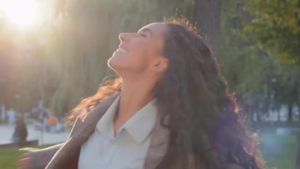 Vista posterior feliz emocionado riendo sonriente de pelo largo rizado morena mujer con hermoso pelo alegre girando girando girando tocando el pelo verde parque al aire libre fondo disfrutando de la vida día — Vídeo de stock