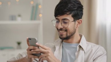 Kapalı mekanda yaşayan, Arap, gözlüklü, gözlüklü, evde oturup sohbet eden, cep telefonu kullanan, haberleri okuyan, akıllı telefonlu, şaşırmış bir adam.