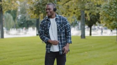 Afro-Amerikan stili, neşeli, tasasız genç, parktaki mutlu adam kulaklık takıyor, cep telefonu kullanıyor, müzik dinliyor, şarkı söylemenin tadını çıkarıyor, davul çalıyor, açık havada dans ediyormuş gibi yapıyor.