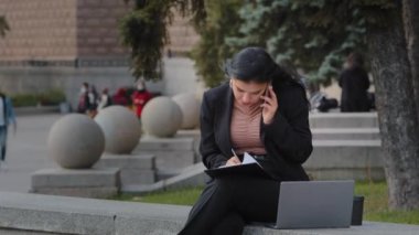 Genç iş kadını dışarıda bilgisayar başında çalışıyor. Cep telefonuyla konuşuyor. İş anlarında kadın, sokakta oturan çok görevli güzel İspanyol kadına veriler yazıyor.