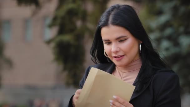 Mulher jovem hispânica sentado na rua abre carta de papel ler boas notícias menina bonita feliz sorrindo fêmea tem sonho de promoção de crescimento de carreira de trabalho na admissão ao trabalho para a universidade recebeu bolsa de estudos — Vídeo de Stock