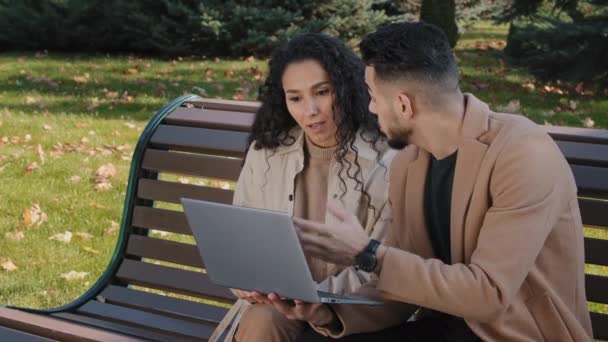 Aufgeregtes hispanisches Paar liest gute Nachrichten auf Laptop auf Bank im Herbst Park erfolgreiche Partner glücklich Umarmung überrascht E-Mail-Gewinner feiern Sieg Lotterie umarmt Frau — Stockvideo