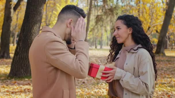 Guy copre gli occhi con le mani ragazza fa regalo inaspettato per l'uomo per compleanno coppia abbraccio all'aperto uomo sorpreso famiglia ispanica felicemente sorridente amanti festeggiare in autunno parco riccio signora abbracciando maschio — Video Stock