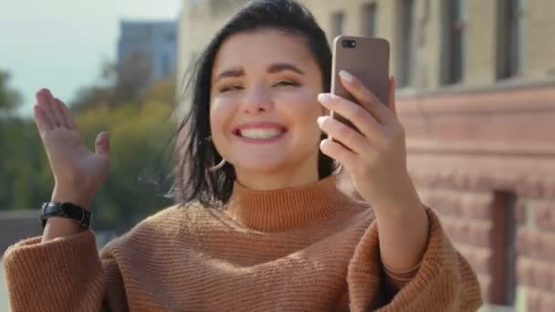 Primer plano feliz joven mujer en la ciudad al aire libre comunicarse por videollamada en línea desde gadget móvil utilizando dispositivo lindo blogger chica hispana de pie en la calle hablando sonriente conferencia por teléfono — Vídeos de Stock