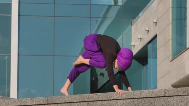 Silny elastyczny sport muzułmanin młoda dziewczyna jogin kobieta robi ćwiczenia ćwiczenia praktyka w mieście asana jogi pozowanie trójnożny pies siedzi na sznurku na tle miasta budynku, elastyczność spokój koncepcja — Wideo stockowe