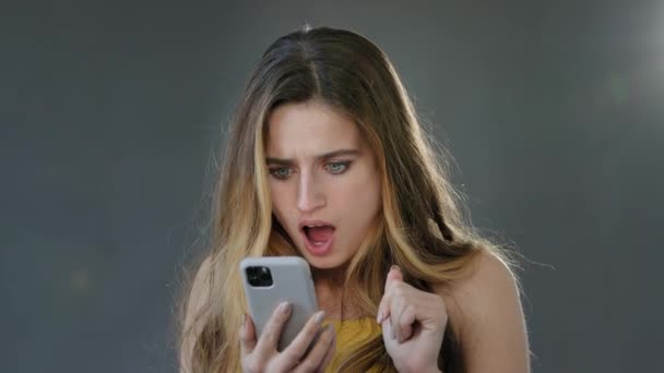 Эмоциональный шок удивлен удивленный блондинка смотрит смартфон дисплей мобильного телефона открытый рот от шока неожиданное получение сообщения с хорошими новостями, студия выстрел изолирован на сером фоне — стоковое видео