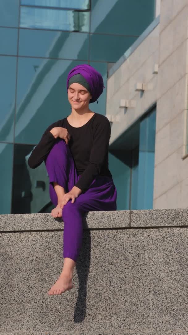 Vertikální pohled veselý šťastný bezstarostný inspirovaný mladý hidžáb dívka islámský muslim bosá klidná žena sedí ve městě budova pozadí venku s úsměvem snění těší moment relaxační odpočinku — Stock video