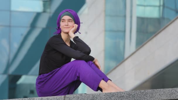 Gyönyörű nyugodt békés lány iszlám muszlim nő mezítláb hölgy nő visel lila hidzsáb ül a városban az utcán épület háttér nézi körül pihentető gondolkodás inspiráció álmodik — Stock videók