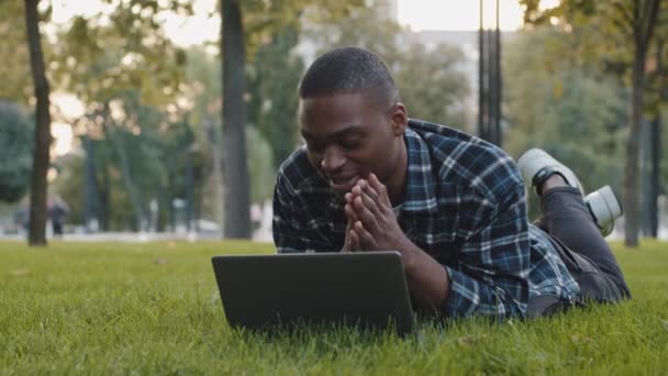 Šťastný africký obchod muž přátelský bezstarostný chlap ležící na trávníku zelené trávy v letním parku s videohovory chat konference komunikující online rozhovor blog mluvení na web kamery venku — Stock video