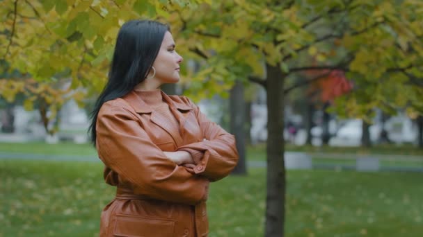 아름다운 젊고 아름다운 젊은 여성 이 가슴을 가로지르는 팔을 바라보며 천천히 도시의 가을 공원에 서 있는 매력적 인 스페인 소녀를 집중적으로 바라본다. — 비디오