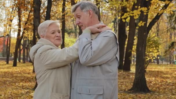 快乐的老夫妇在秋天的公园里跳舞享受浪漫的舞伴爱着中老年爷爷奶奶在户外，闷热的丈夫拥抱着腰，可爱的妻子在聊天，开心的笑着 — 图库视频影像