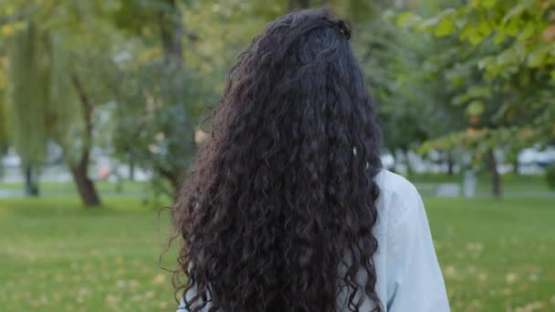 Gros plan arrière vue islamic brune avec luxueux long bouclé noir sombre cheveux sains marche dans le parc dans la nature à l'extérieur en se retournant en regardant la caméra avec sourire dents sourire sincèrement en riant — Video