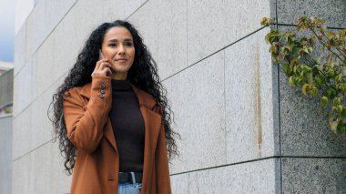 Portre mutlu Latin kız iş kadını uzaktan konuşma şehirde yürürken cep telefonuyla konuşma. Dışarıya çıkan akıllı telefonla konuşan bir bayan.