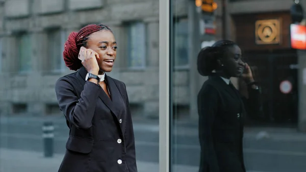 Cep telefonundan konuşan Afro-Amerikalı iş kadını dışarıda ofise gidiyor. Akıllı telefon dijital uygulama kullanan ciddi bir afro kız işadamı. Şehir caddesinde yürüyüş çağrısına cevap veriyor. — Stok fotoğraf