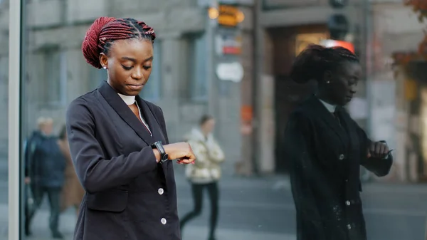 Genç iş kadını Afro-Amerikan bayan şirket binasının yakınında yürüyor görüşme için geç kalıyor şehirdeki caddelerde hareket halindeki kol saatlerine bakıyor. — Stok fotoğraf