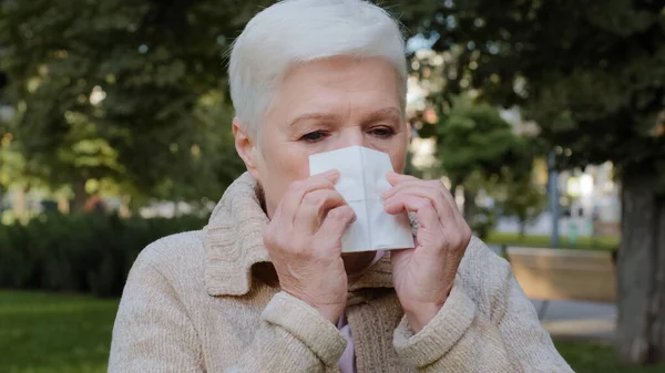 Allergic middle-aged lady feels unwell having flu symptom, ill old mature woman hold tissue sneezing got fever caught cold blowing running nose in handkerchief, sick. Allergy concept, closeup view — Stock Photo, Image