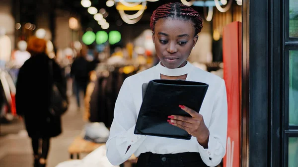 Poważne skupiony młody Afryki dziewczyna sprzedawca kobieta pracownik zajęty kobieta sklep odzieżowy właściciel stoi w pomieszczeniach za pomocą tabletu cyfrowego urządzenia bezprzewodowego gadżet do inwentaryzacji produktów online stronie internetowej — Zdjęcie stockowe