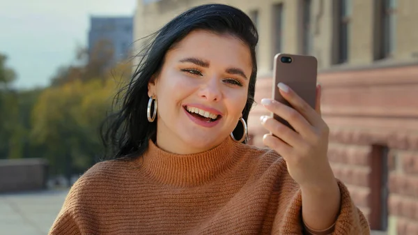 Closeup happy young woman in city answer video call attractive girl make photo using telephone device beautiful female portrait talking to friends colleagues with mobile phone conference chat on — 图库照片