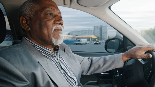 Old african american man driving car serious pensive elderly male leaves parking lot mature businessman looking closely at road drives up approaches intersection experienced driver ride on highway — 图库照片