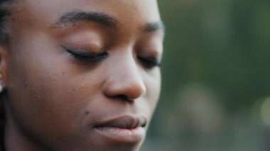 Aşırı yakın plan kadın yüzü, doğal makyajı, koyu teni, Afro-Amerikan kadın açık havada, gözleri kapalı dua etmeyi, görme problemleri olduğunu düşünerek duruyor.