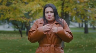 Sonbahar parkında donarak soğuktan donan, kolları çaprazlanmış, düşük hava sıcaklığından rahatsız olan, soğuk algınlığından titreyen genç İspanyol bir kadın.