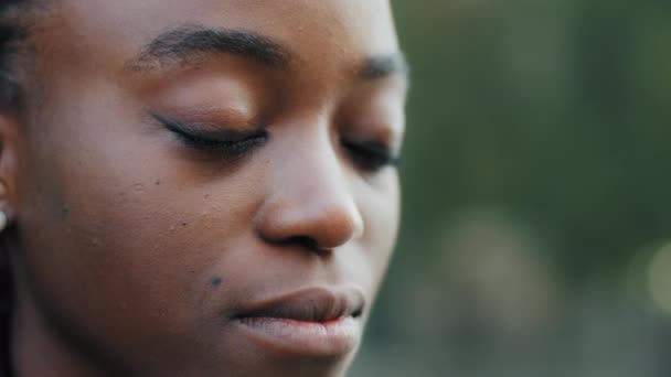 Extreme close-up γυναικείο πρόσωπο με φυσικό μακιγιάζ τέλειο ακόμη και σκούρο δέρμα, αφρικανικής Αμερικής γυναίκα νεαρή κοπέλα κυρία στέκεται έξω σε εξωτερικούς χώρους με κλειστά μάτια όνειρα σκέψης προσεύχεται, προβλήματα όρασης — Αρχείο Βίντεο