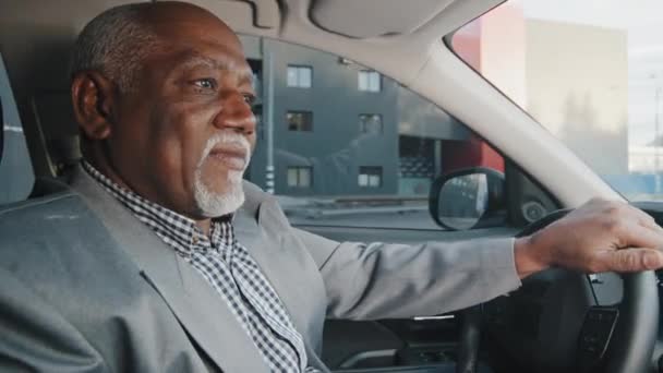 Old african american man driving car serious pensive elderly male leaves parking lot mature businessman looking closely at road drives up approaches intersection experienced driver ride on highway — 图库视频影像