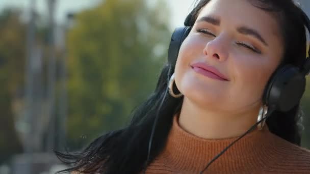 Portret tânără femeie fericită în aer liber în căști ascultând muzică preferată folosind smartphone-ul fără griji fată hispanică zâmbind dansând la melodie plăcută sunet audio de sex feminin bucurându-se de viață — Videoclip de stoc