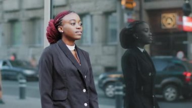 Genç iş kadını Afro-Amerikan bayan şirket binasının yakınında yürüyor görüşme için geç kalıyor şehirdeki caddelerde hareket halindeki kol saatlerine bakıyor.