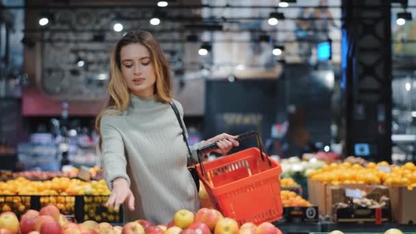 Młody biznes kobieta dziewczyna nabywca klient blondynka pani konsument stoi w sklepie w pobliżu licznika z owoców w supermarkecie spożywczym wybierając soczyste dojrzałe jabłka dla soku dieta zakup żywności stawia w koszyku — Wideo stockowe