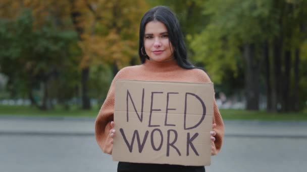 Close-up beautiful hispanic young woman stands on street near roadway unemployed girl holding cardboard banner NEED WORK female smiling shyly feeling awkwardness financial problems crisis dismissal — Vídeo de Stock