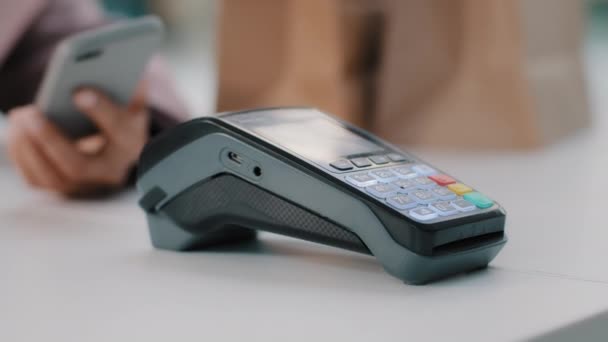 Woman at check-in desk at counter pays with smartphone through NFC contactless payment from mobile phone in bar cafe purchase of food products pay by card from telephone close-up focus on terminal — Video Stock