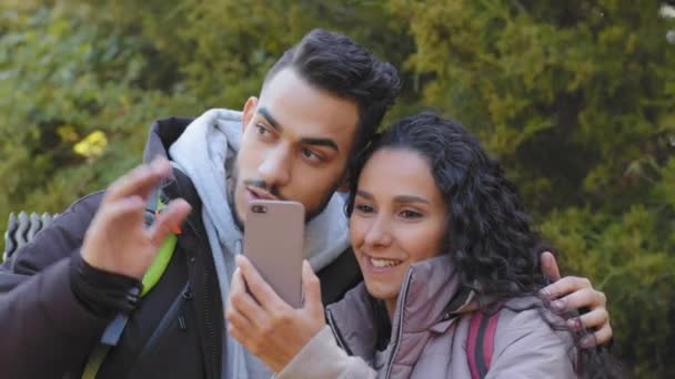 Multiracial couple of young newlyweds walking in autumn forest making video call using smartphone looking for way make up route. Millennial cheerful travelers spending weekend time outdoor together — Vídeo de Stock