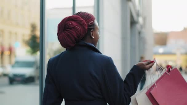 Voltar ver feliz bonito elegante elegante mulher americana africana senhora consumidora andando na cidade perto de shopping center edifício com compras pacotes girando sorrindo olhando para a câmera — Vídeo de Stock