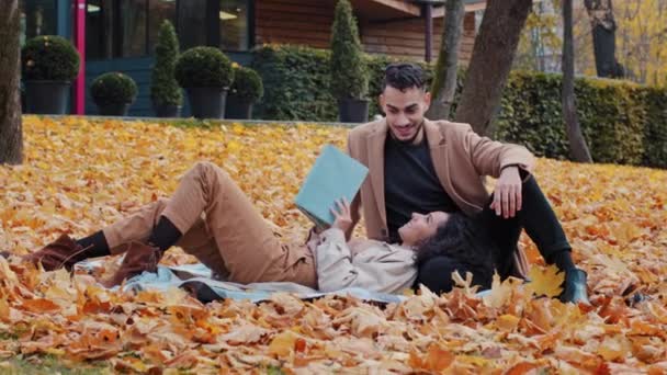 Ημερομηνία σε εξωτερικούς χώρους νεαρός γενειοφόρος Άραβας άντρας ειλικρινά μιλάμε με αγαπημένη γυναίκα άντρας γνέφει εγκρίνοντας όμορφο κορίτσι που βρίσκεται σε καρό σε κίτρινα φύλλα διαβάζοντας το βιβλίο ευτυχισμένο ζευγάρι χαμογελώντας μαζί στο πάρκο φθινόπωρο — Αρχείο Βίντεο