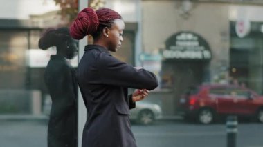 Güzel, şık, modaya uygun genç bir bayan model siyahlı Afrikalı bir Amerikalı kadın binanın yakınındaki caddede yürüyor, kol saatine bakıyor.