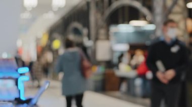 Bulanık manzaralı arka planda gezen insanlar, alışveriş merkezi alışverişçileri, tıbbi maske takan adam. Satış konsepti. Marketteki alıcılar mağazadan kıyafet satın alıyorlar.