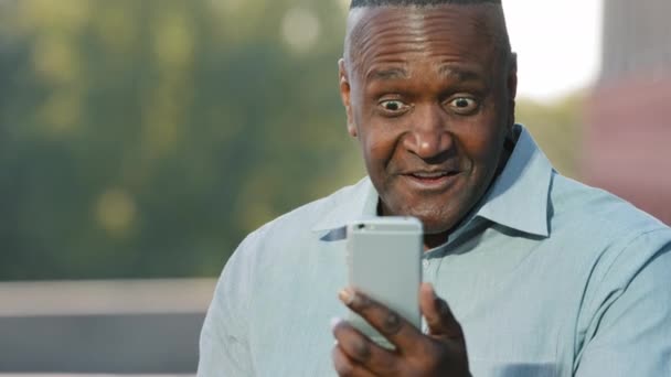 Äldre amerikanska mannen som håller smartphone tittar på skärmen under videochatt känslomässigt samtal delar nyheter med samtalspartner, håller med säger ja, förvånad, vägrar visar inget fall gest för hand — Stockvideo