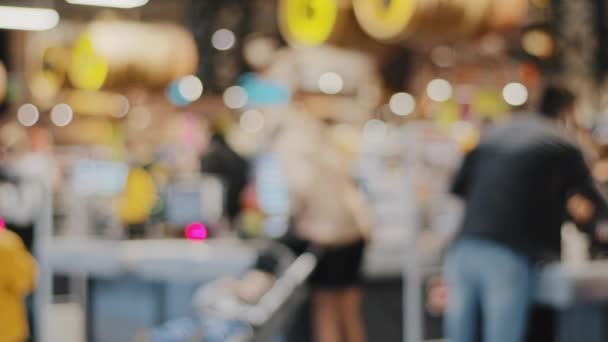 Blurred view unfocused unrecognizable people in store man and woman shoppers consumers customers at checkout in supermarket shopping mall buying groceries food standing at queue paying money — Stock Video