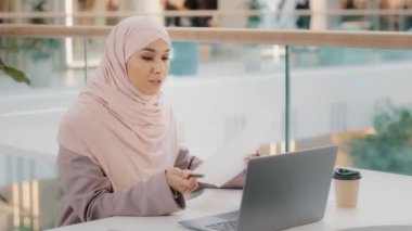 Genç İslami kadın kafeteryada oturmuş video konferansında sohbet ediyor. Laptop mesafesindeki tesettürlü müslüman kız internet kamerasındaki uzaktan görüşmede müşteriyle pazarlık yapıyor.