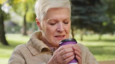 Emeklilik yaşının zarif büyükannesi parkta oturmuş çay içiyor. Olgun bir kadın dinleniyor, tek kullanımlık bardakta aromatik sıcak kahvenin tadını çıkarıyor. Yaşlı bayan dışarıda vakit geçiriyor.