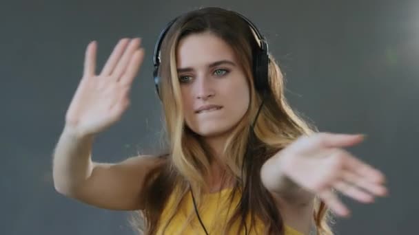 Retrato femenino joven alegre bailando mujer milenaria dama rubia modelo danza escuchando música con auriculares cantando canción audio sonido alegría mirando a la cámara de pie sobre fondo gris estudio — Vídeo de stock