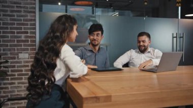 Üç iş ortağı yeni proje geliştiriyor. Çok uluslu iş arkadaşları gülümsüyor konferans odasında sohbet ediyorlar. Patron sunum için dizüstü bilgisayarını kullanıyor.